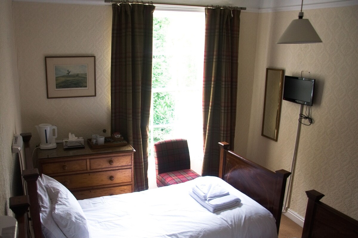 A hotel room with a bed, a desk, a chair, a television, and a window with curtains.