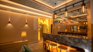 Una zona de bar moderna con encimera de mármol, taburetes, iluminación colgante y un rincón de estar con sofá y lámpara.