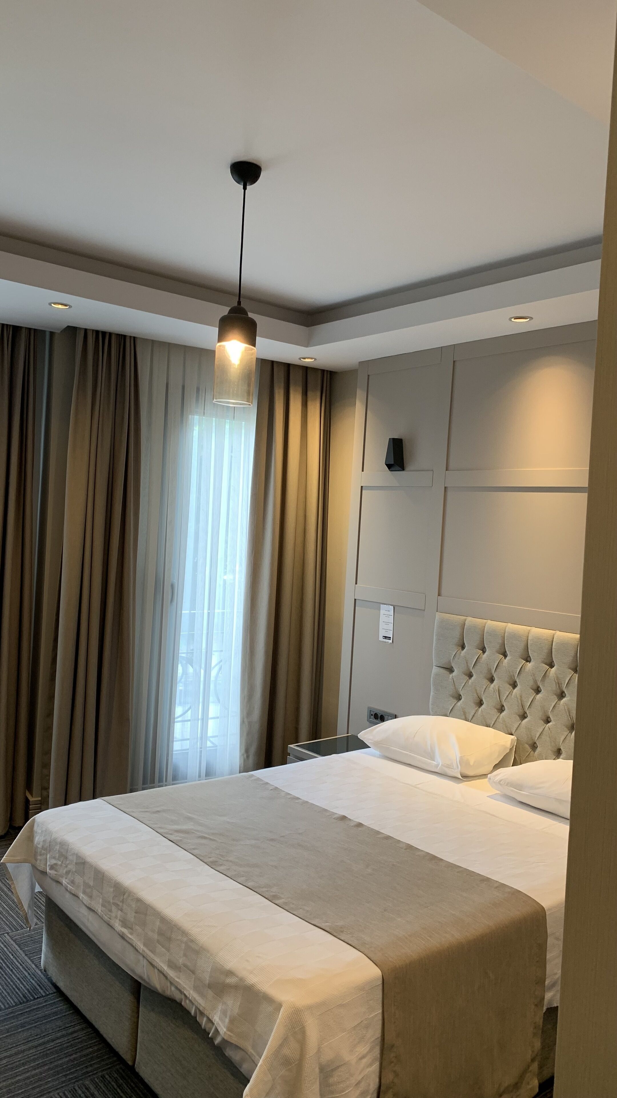 A hotel room with a large bed, a headboard, a bedside table, and a hanging light fixture.