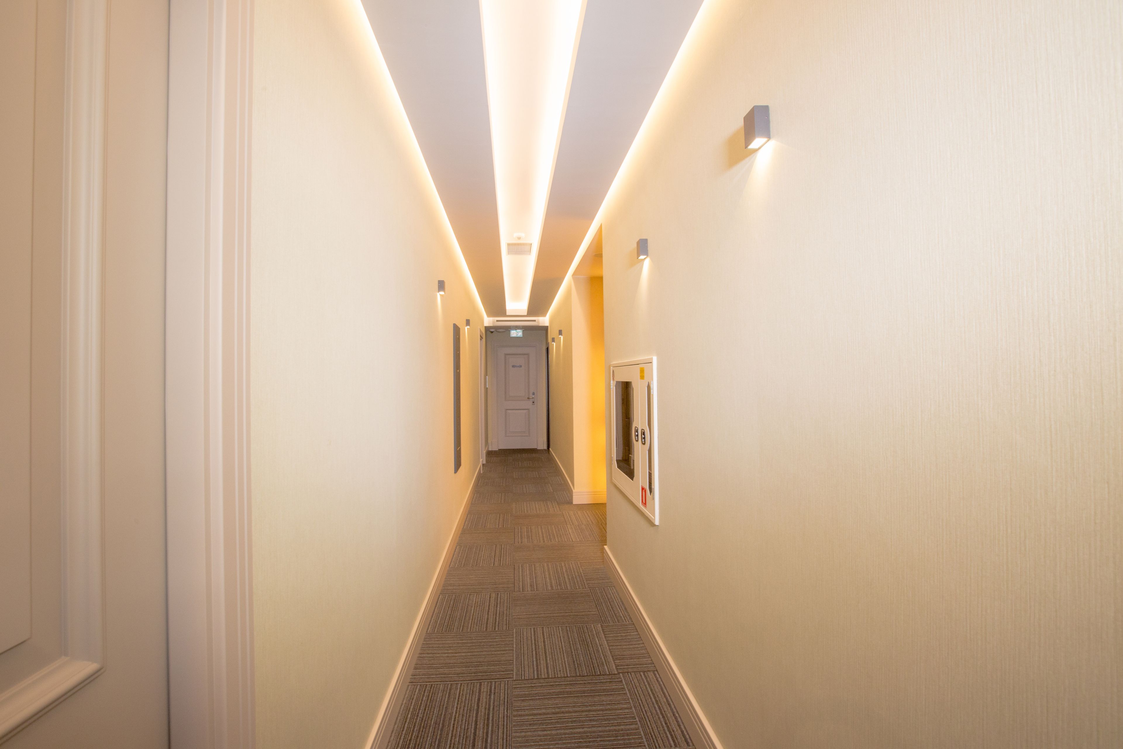 A narrow hallway with a carpeted floor, recessed lighting, and a door at the end.