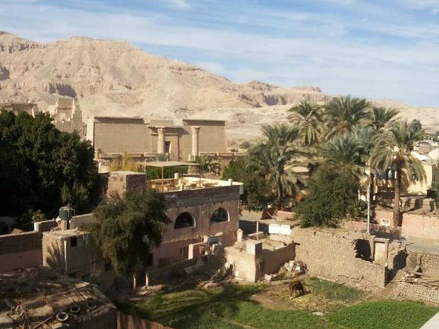 A traditional building with arched windows and a flat roof, surrounded by palm trees and a desert landscape.