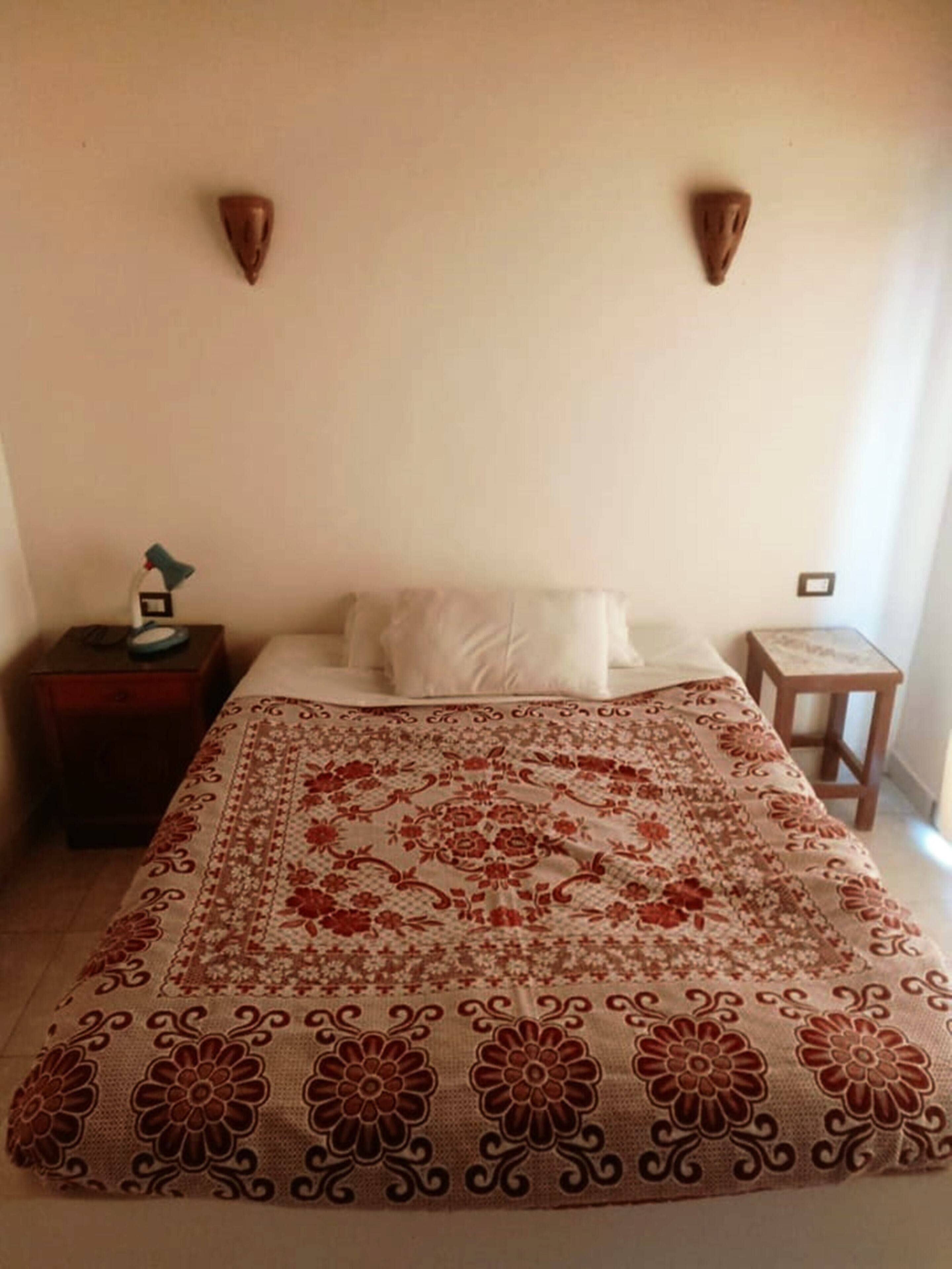 A bedroom with a bed, a nightstand, a lamp, and a wall-mounted light fixture.