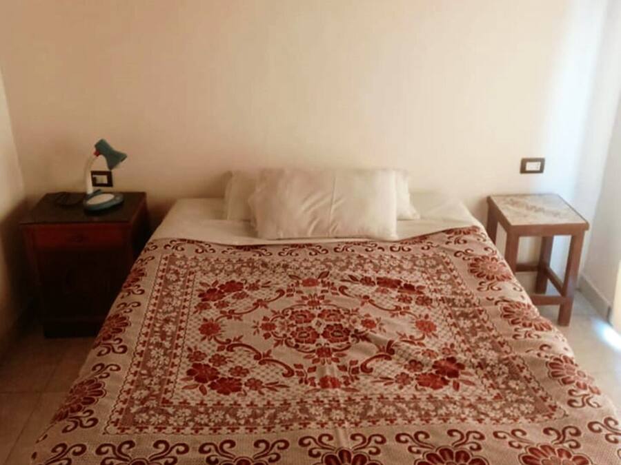 A bedroom with a bed, a nightstand, a lamp, and a wall-mounted light fixture.