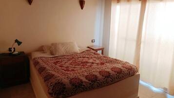 A bedroom with a bed, a nightstand, a lamp, and a window with curtains.