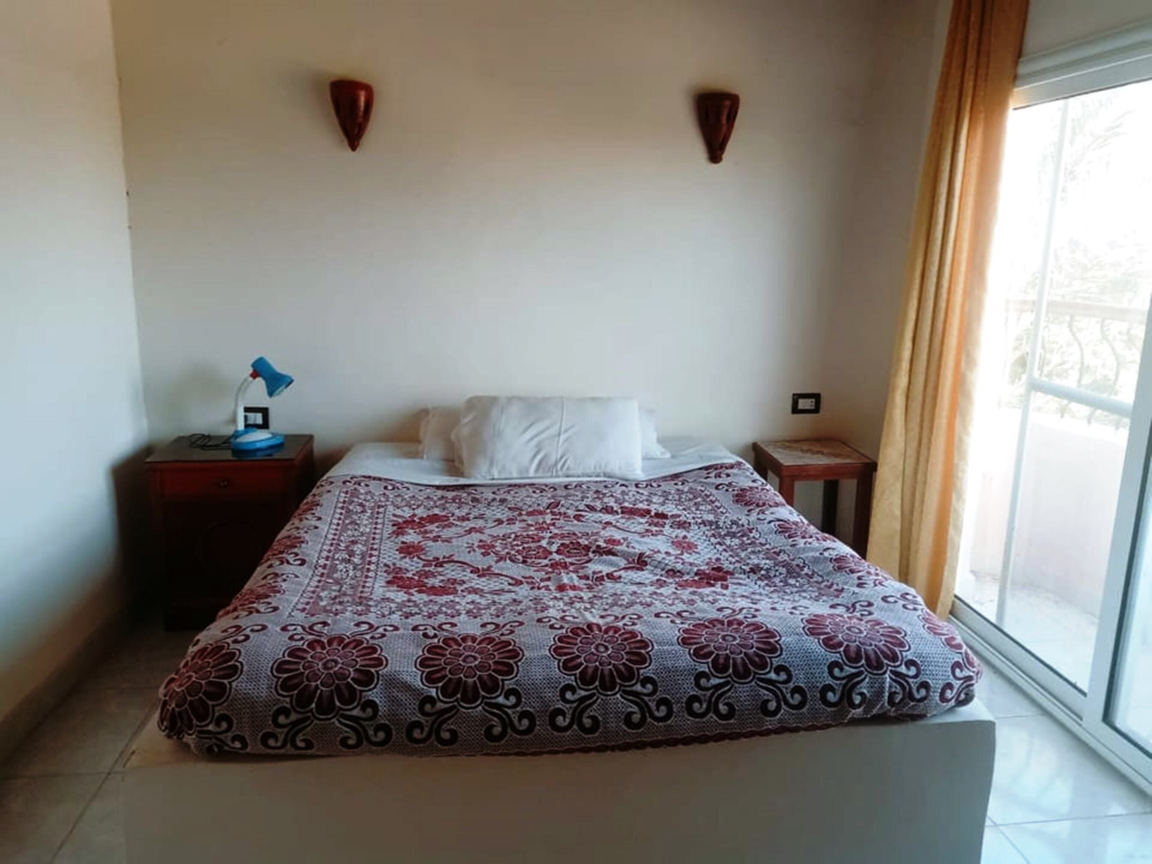 Una habitación de hotel con cama, una mesita de noche con lámpara y ventana con cortinas.