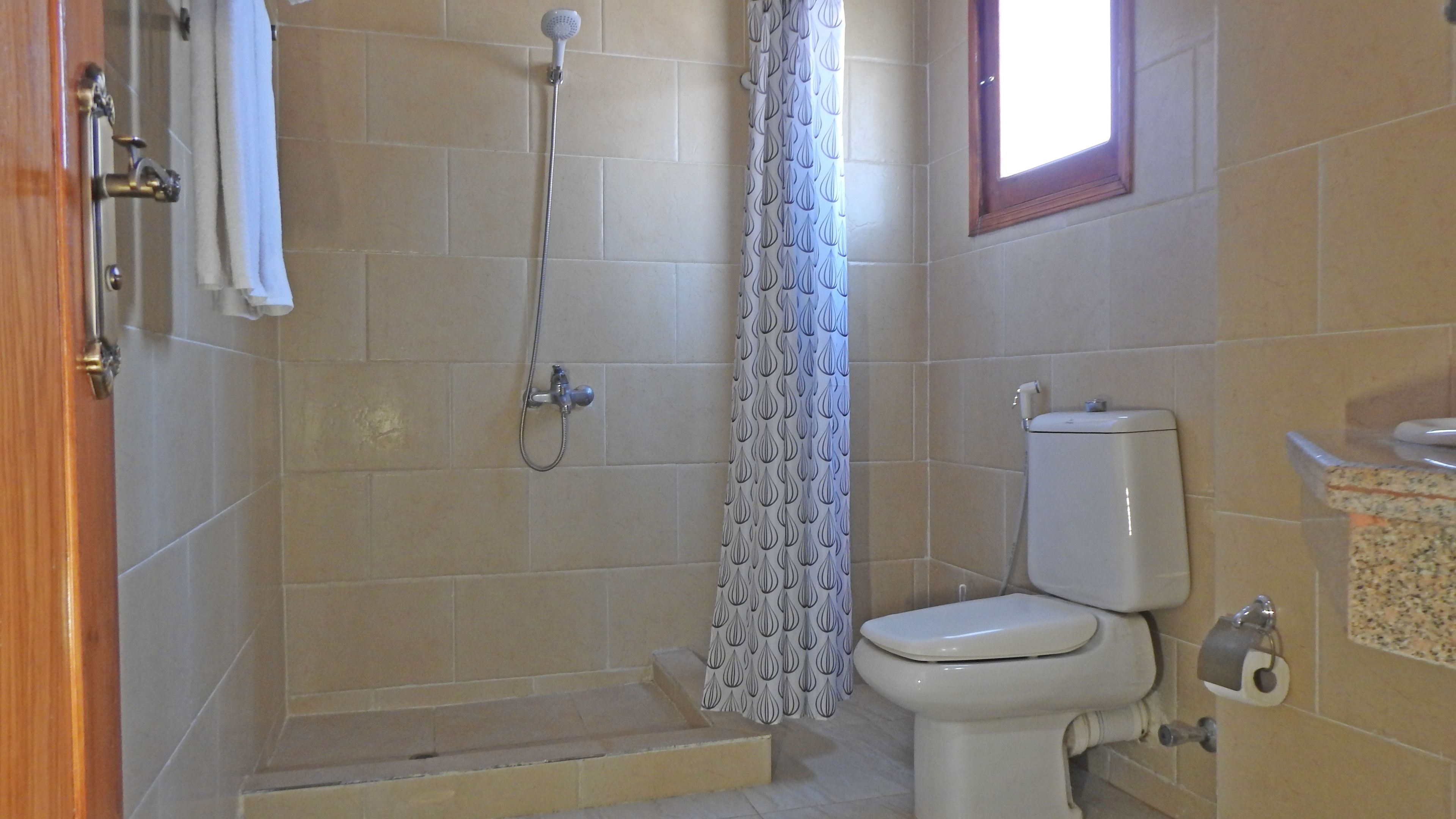 Un baño con ducha, inodoro y ventana.