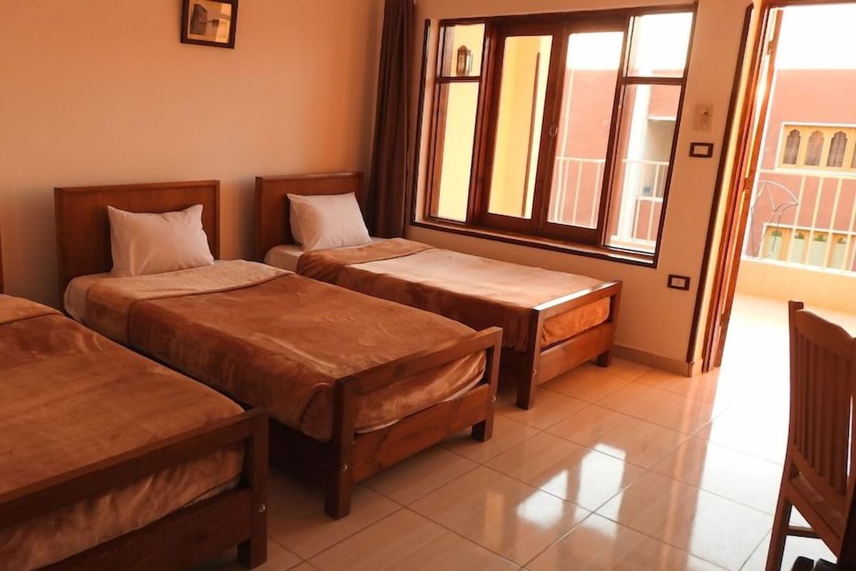 A hotel room with three wooden beds, a window with a view, and a tiled floor.