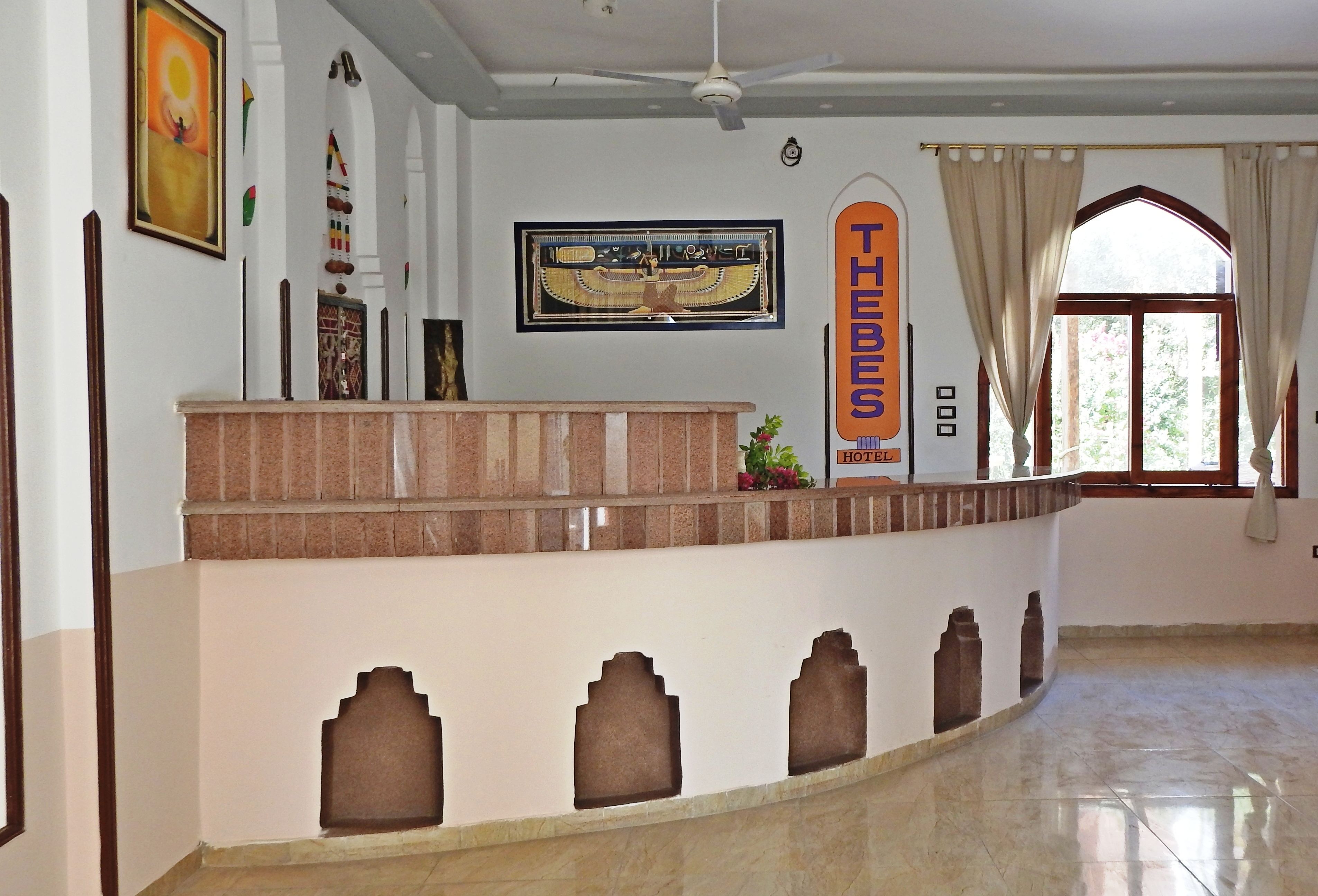A hotel reception area with a marble counter, a large framed artwork above the counter, and a window with curtains.