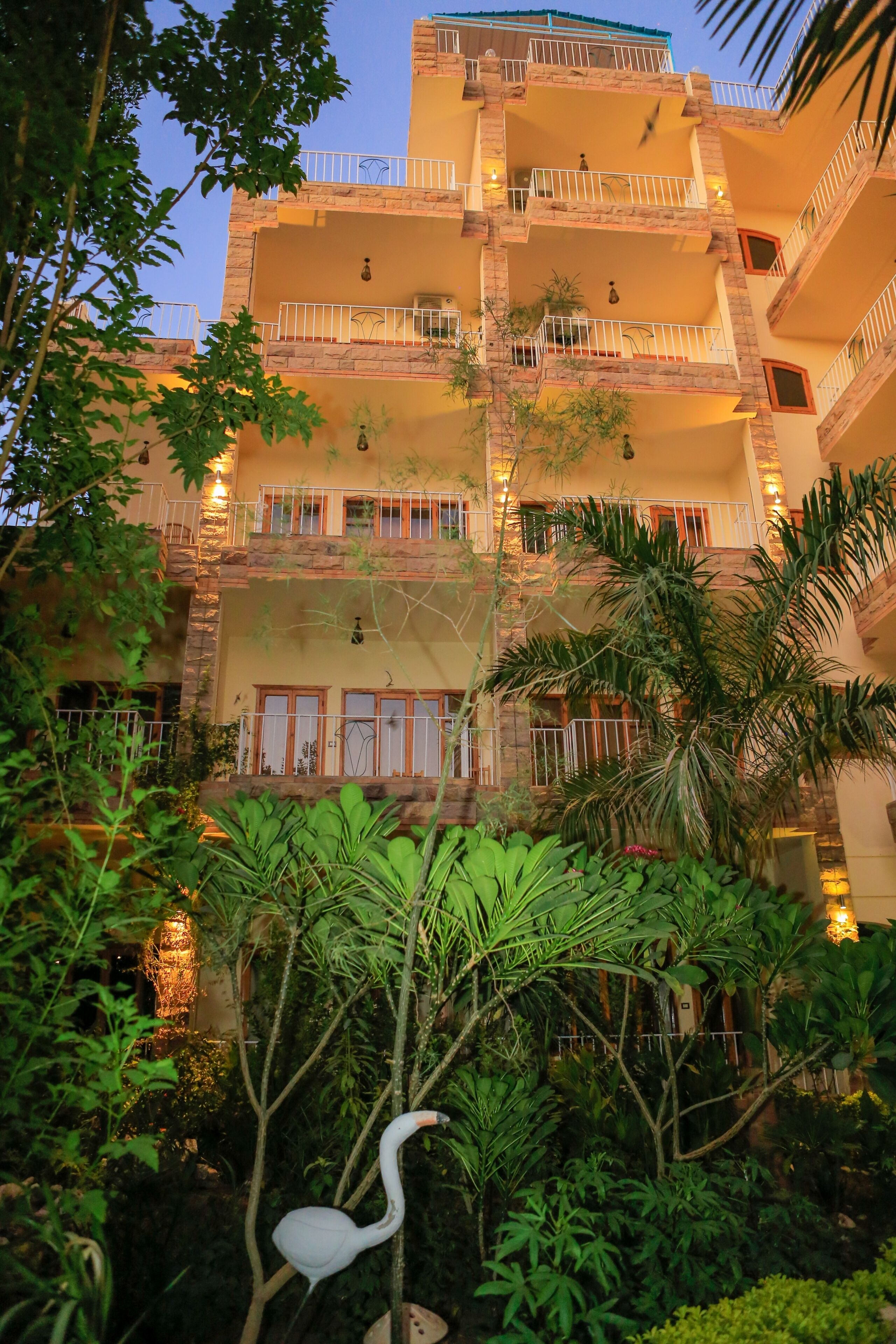 A multi-story building with balconies, surrounded by lush greenery and a white bird.