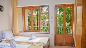 A hotel room with two beds, a balcony with a view of greenery, and a wooden door. - Thebes Hotel Luxor (Luxor)