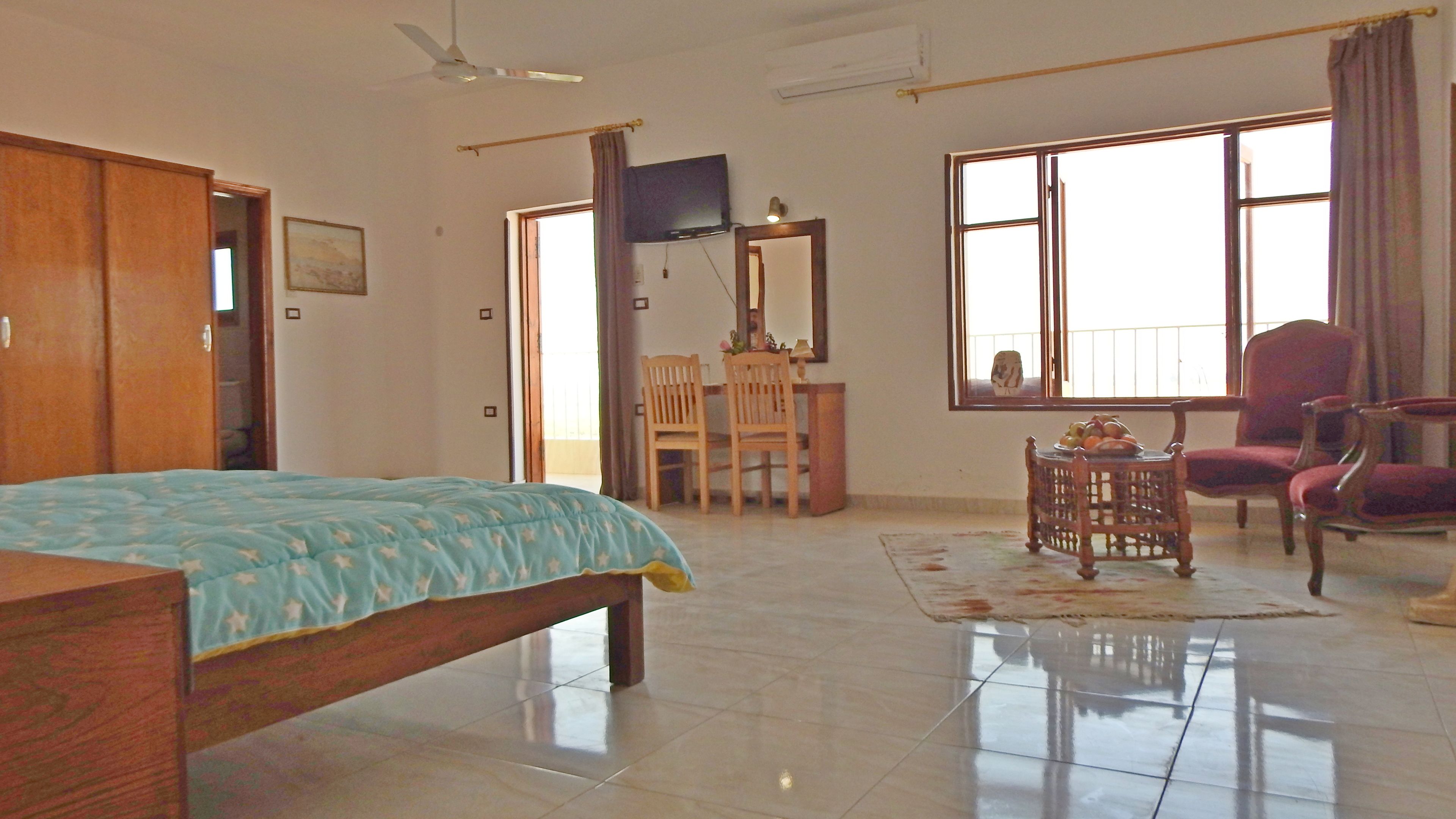 A room with a bed, a desk, a chair, a TV, and large windows.