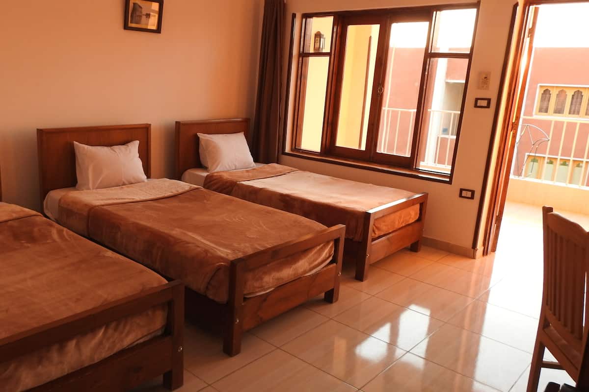 A room with three wooden beds, a window with curtains, and a view of buildings outside.