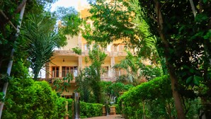 A courtyard with a pathway leading to a building with balconies, surrounded by lush greenery and trees. - Thebes Hotel Luxor (Luxor)