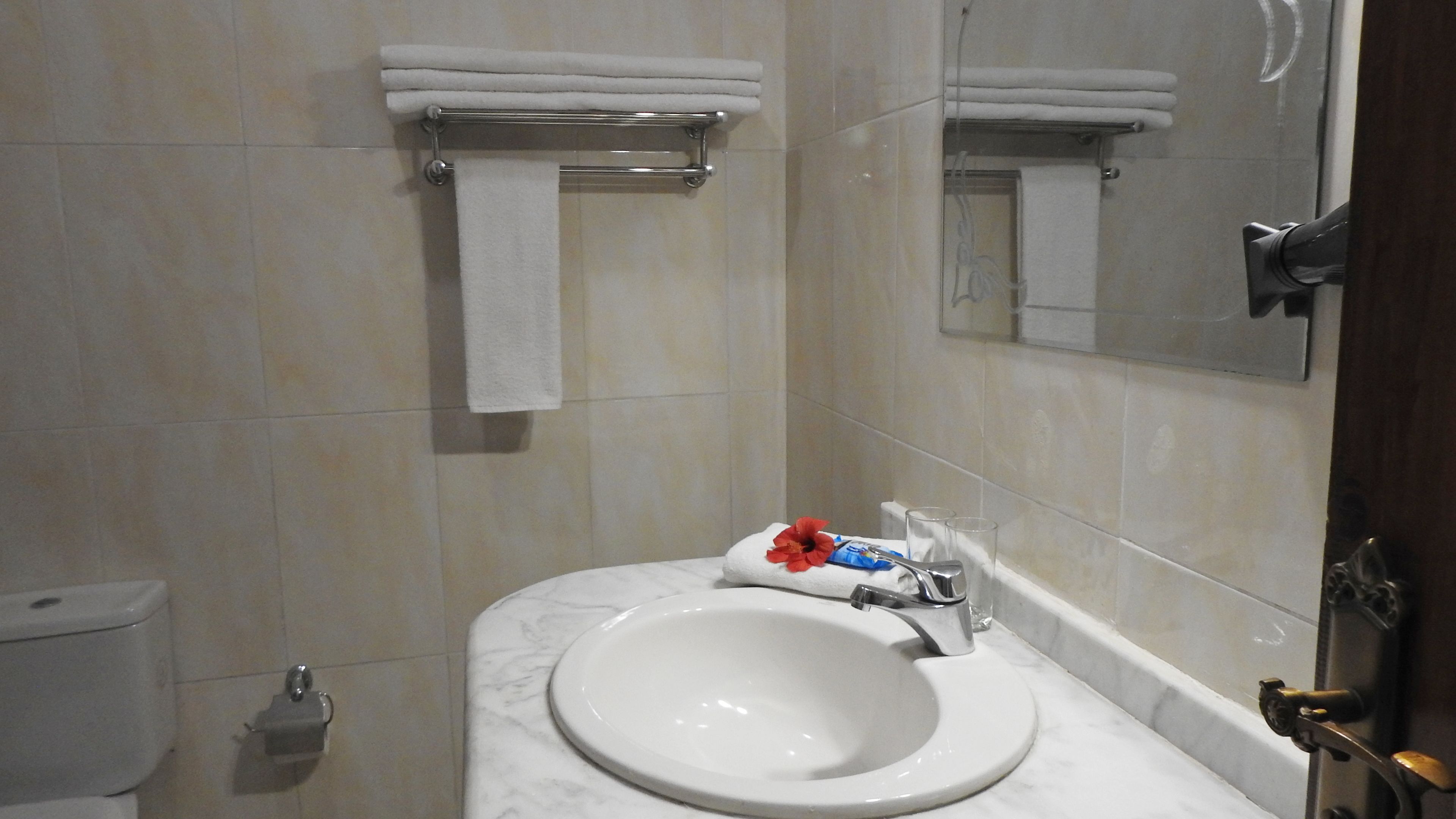 A bathroom with a white sink, a mirror, and a towel rack with folded towels.