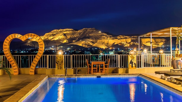 A swimming pool with a heart-shaped sign, a table and chairs, and a view of mountains at night. - Thebes Hotel Luxor (Luxor)