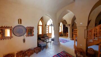 A spacious interior with high arched ceilings, a central seating area with a table and chairs, and a bookshelf in the background.