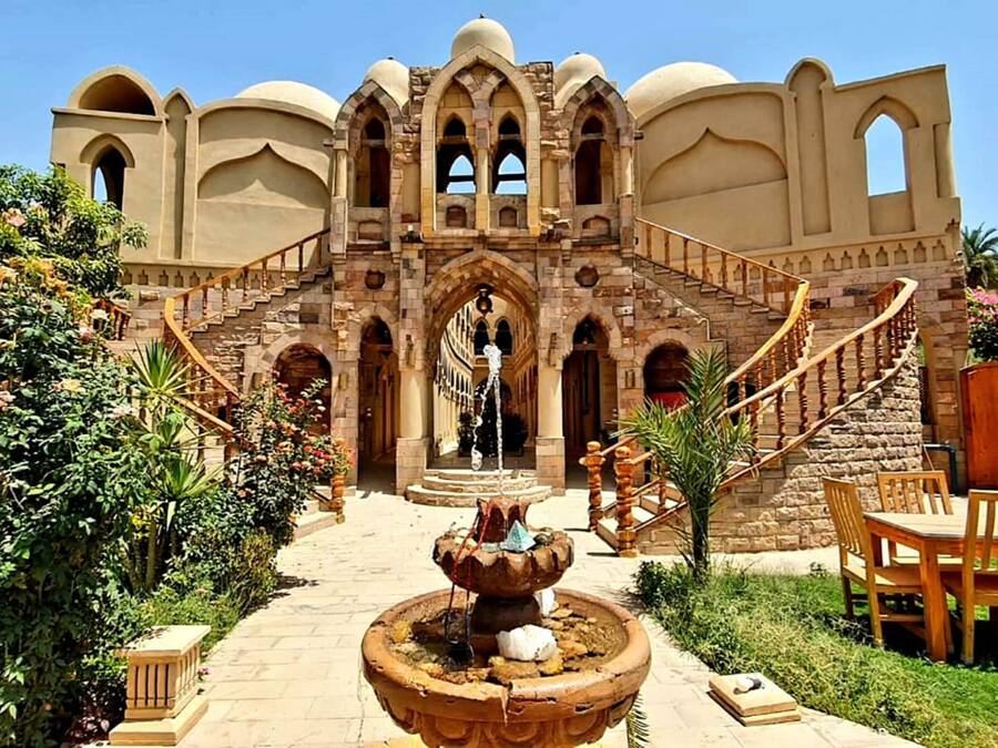 A historic building with a grand staircase, a central fountain, and lush greenery.