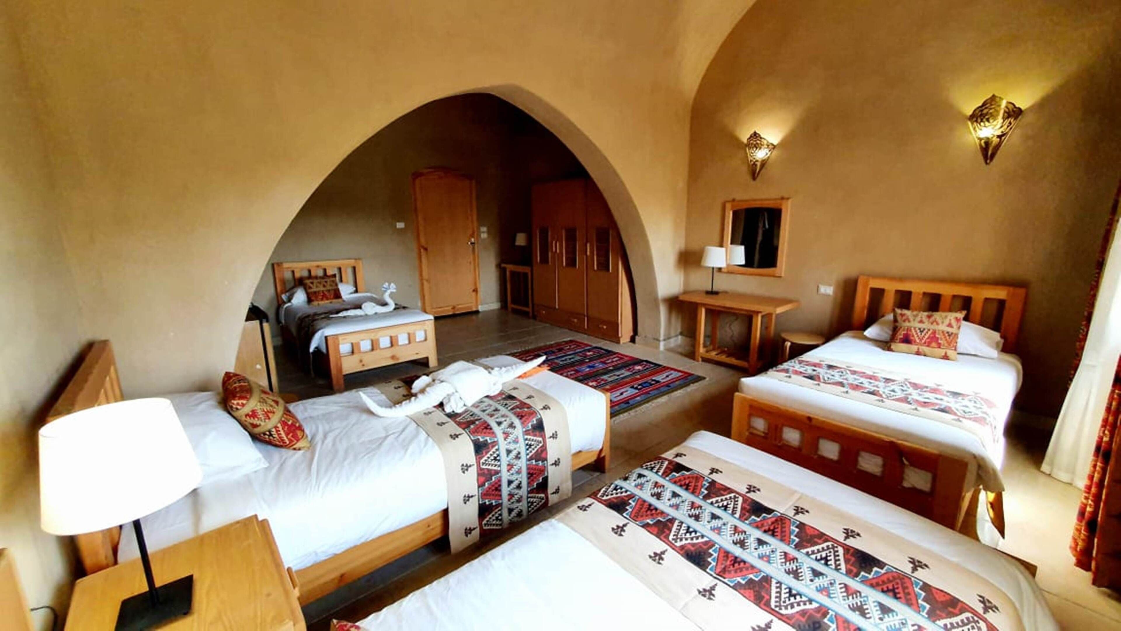 Een hotelkamer met vier bedden, houten meubels en een grote, gebogen deuropening.