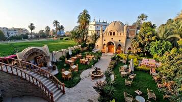 A courtyard with outdoor seating, a fountain, and a large building with a dome and arches.