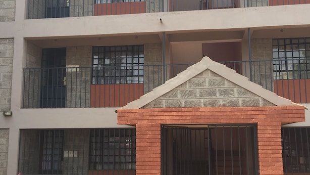 Un edificio de varios pisos con una entrada central, balcones y ventanas protegidas con rejas.