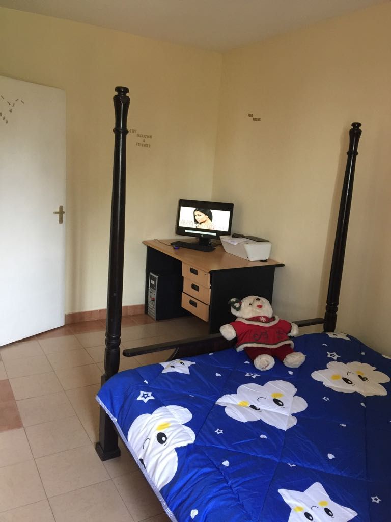 A bedroom with a four-poster bed, a desk with a computer, and a stuffed toy on the bed.