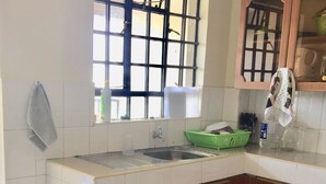 Una cocina con baldosas blancas, un lavamanos, un ventanal con diseño de cuadrícula y armarios de madera.