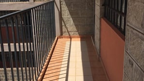 Un balcón estrecho con suelo de baldosas y barandilla metálica.