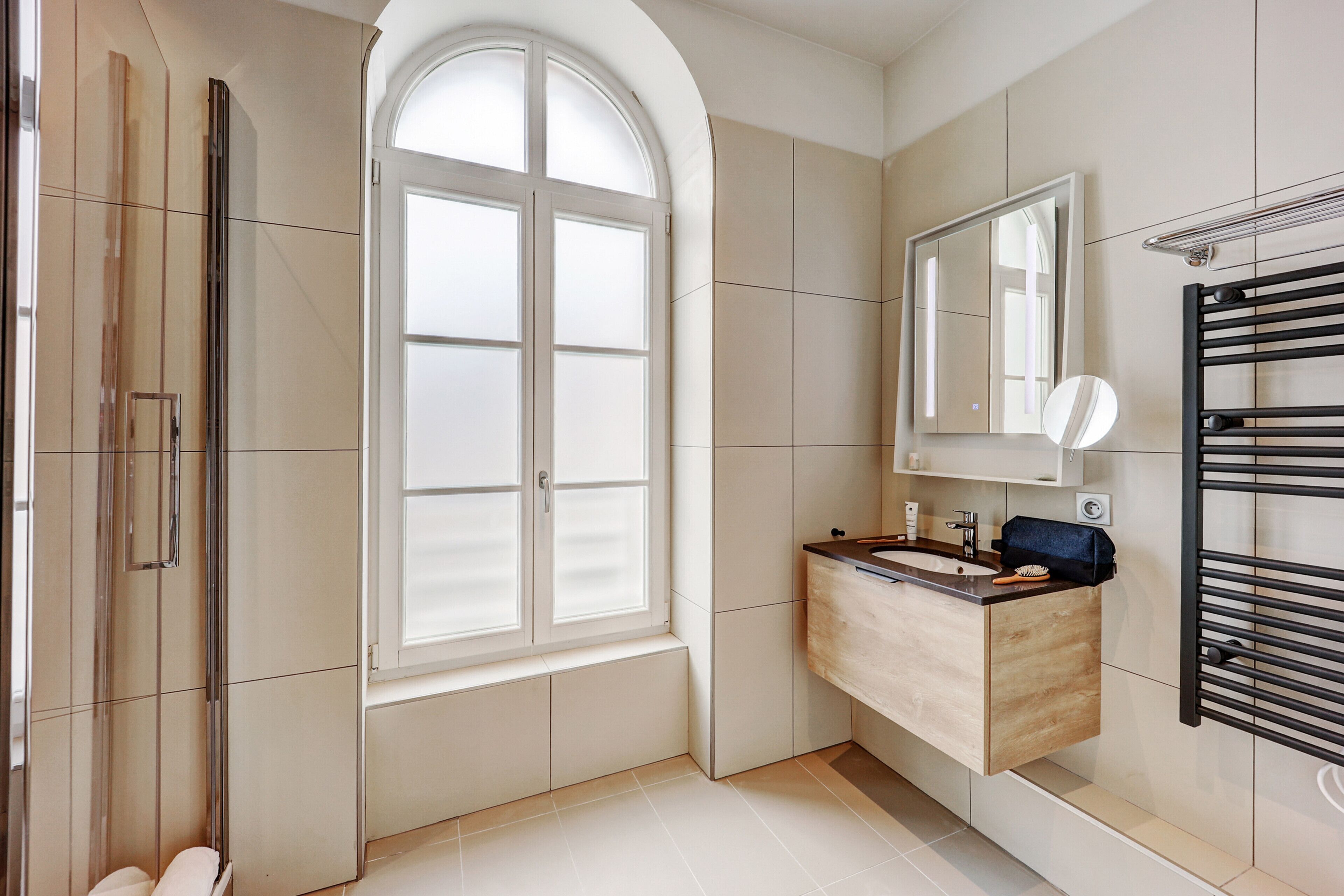 Un bagno moderno con una grande finestra ad arco, una doccia integrata, un mobile lavabo con specchio e un portasciugamani.