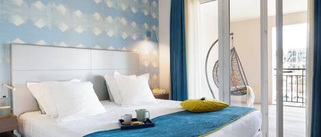 Habitación de hotel con cama, una bandeja con taza y galletas, una silla colgante y vistas al exterior.