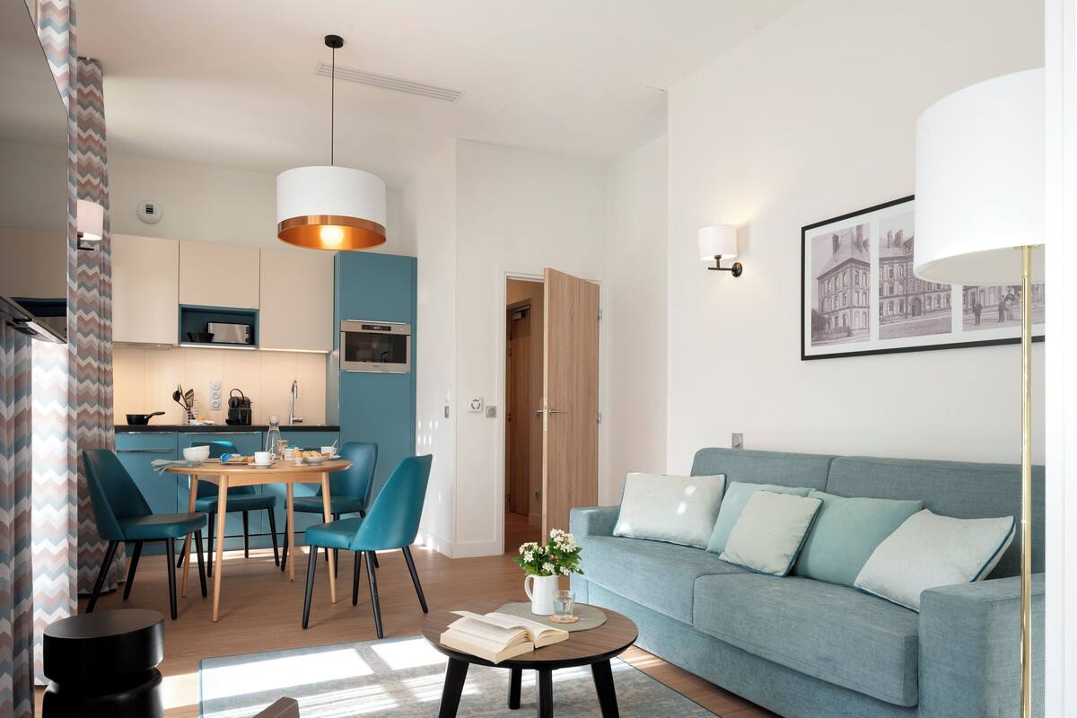 Uma sala de estar moderna com um sofá, uma mesa de centro com um livro e uma área de jantar com cadeiras e uma mesa.