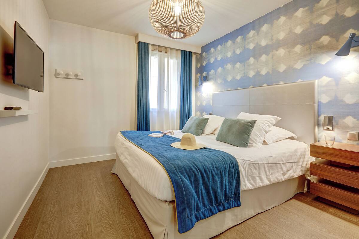 Quarto com cama, televisão, mesa de cabeceira e luminária na parede.