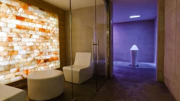 bathroom area with a mosaic-tiled wall and glass partition, featuring a chair and ottoman for relaxation.