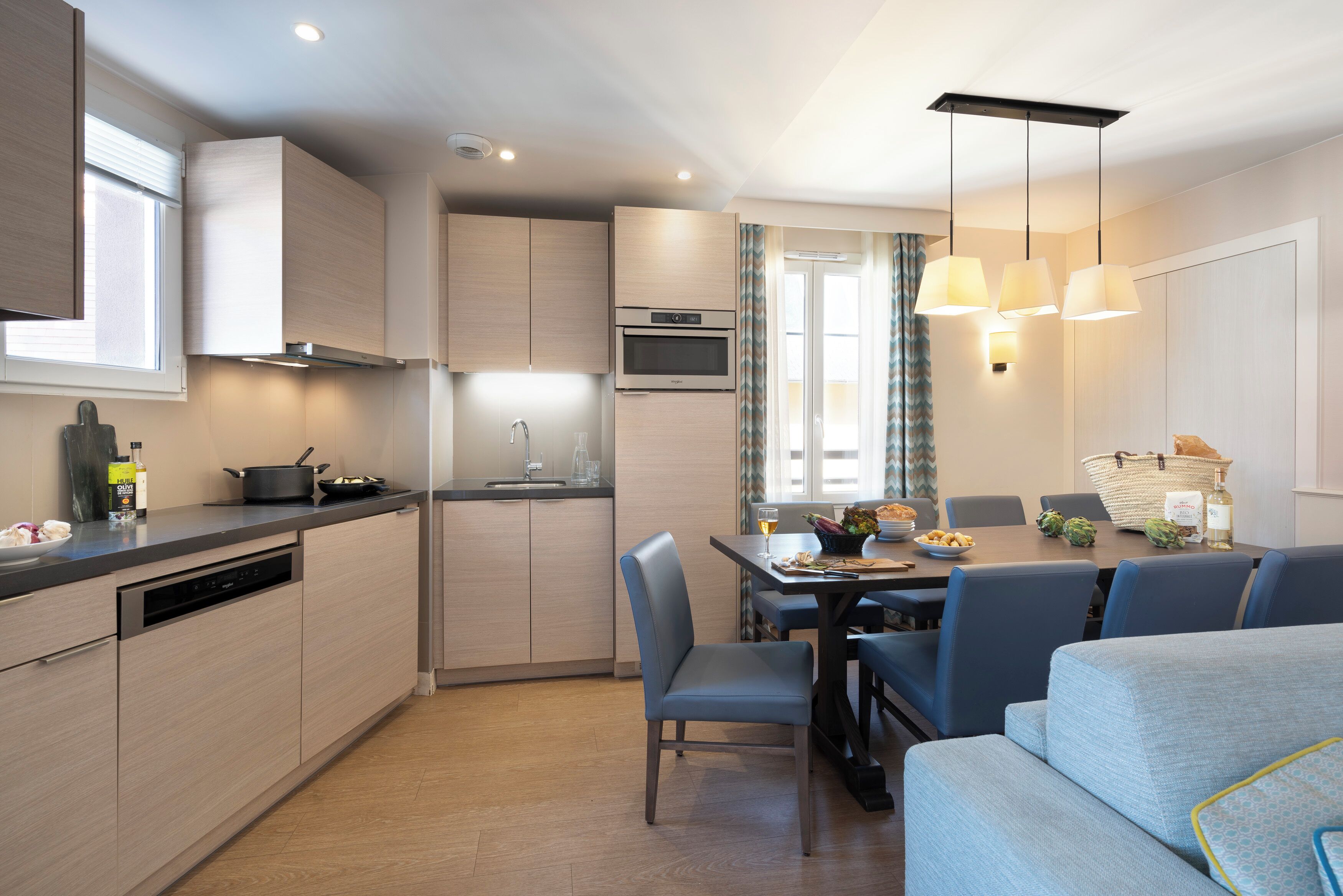 A modern kitchen with built-in appliances, a dining area with a table and chairs, and a sofa in the foreground.