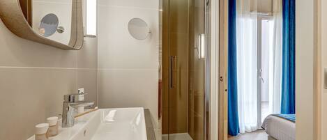 A modern bathroom with a large mirror, a sink with two faucets, and a glass-enclosed shower.