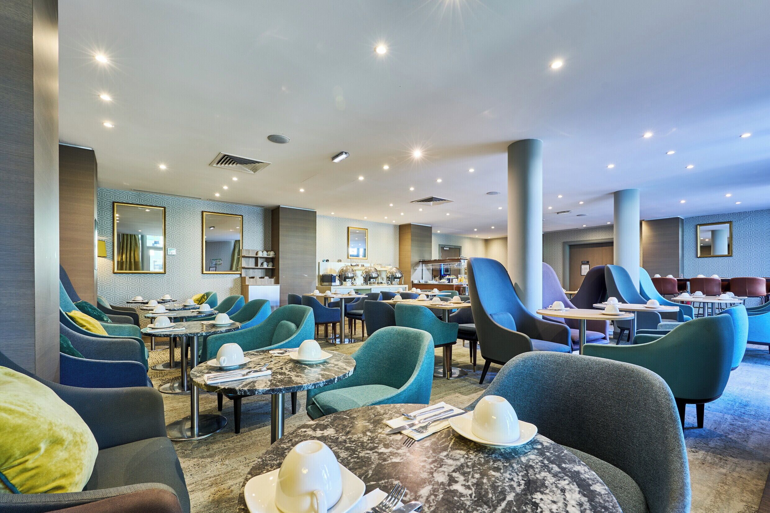Et hotel lobby med flere siddeområder, borde og et stort spejl.