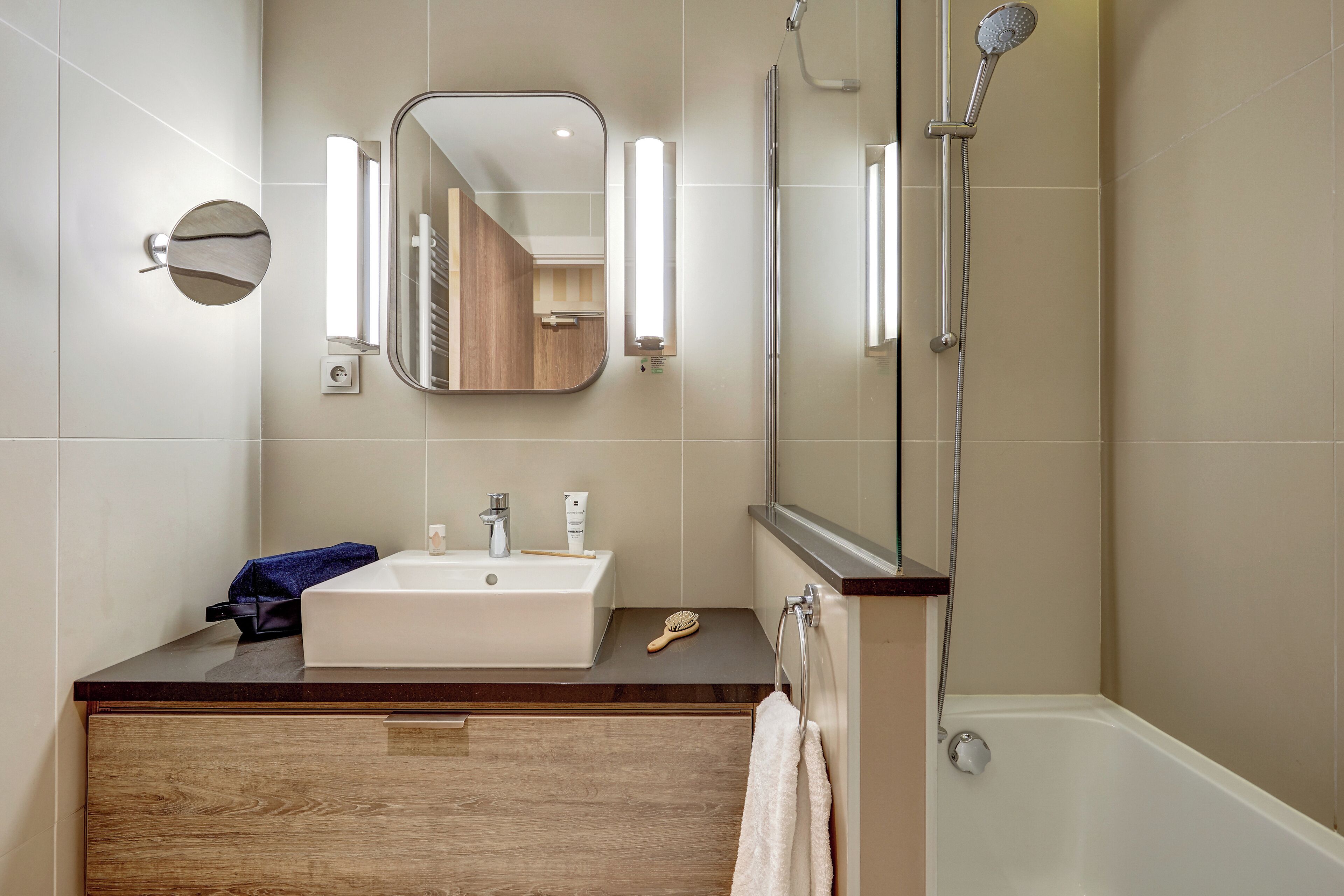A modern bathroom with a wooden vanity, a large mirror, a white sink, and a glass-enclosed shower area.