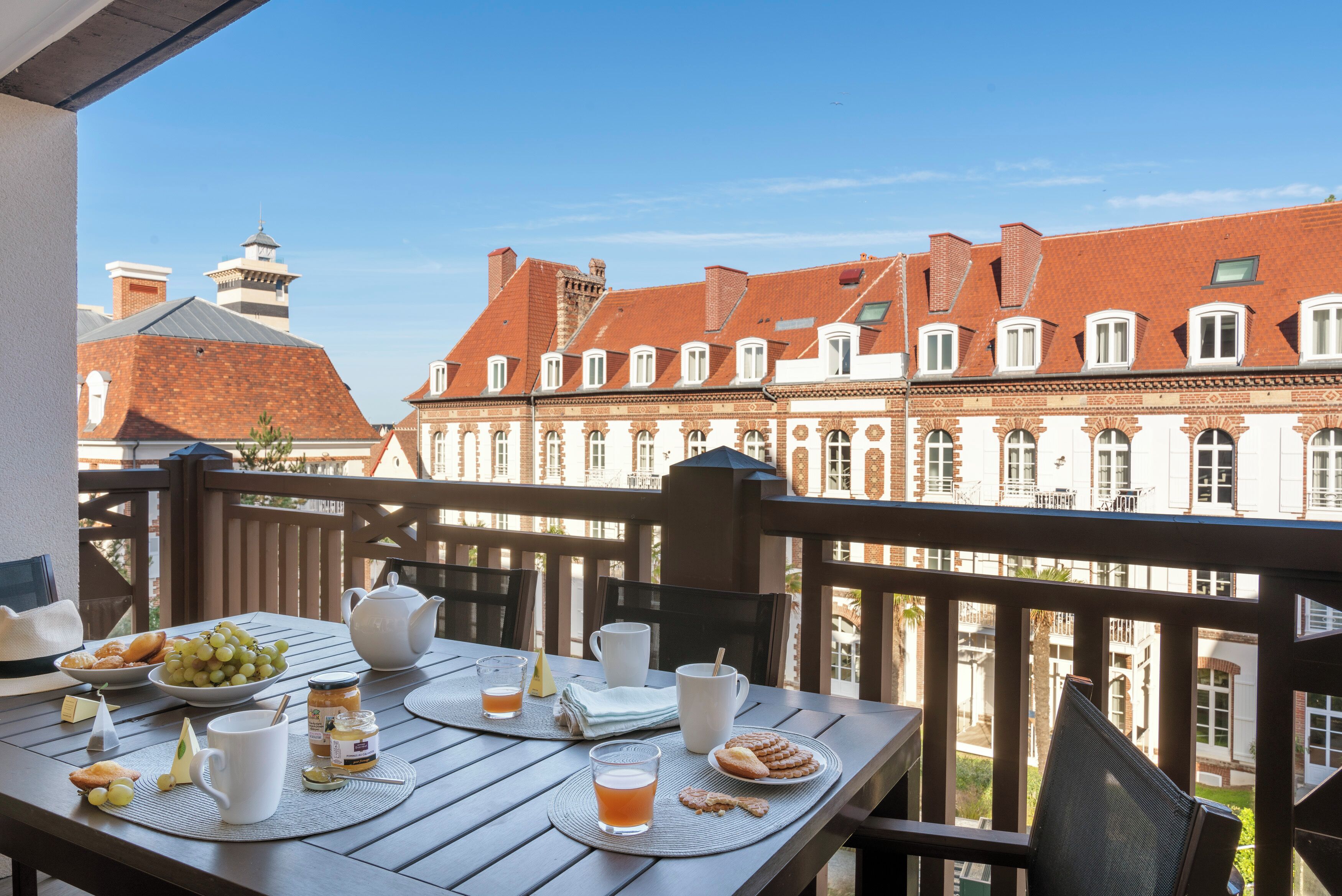 A balcony with a table set for breakfast, including bread, fruit, and beverages.