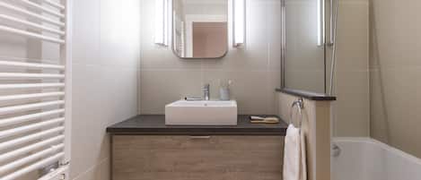 Un baño moderno con un lavamanos blanco, un mueble de madera y una ducha con mampara de vidrio.