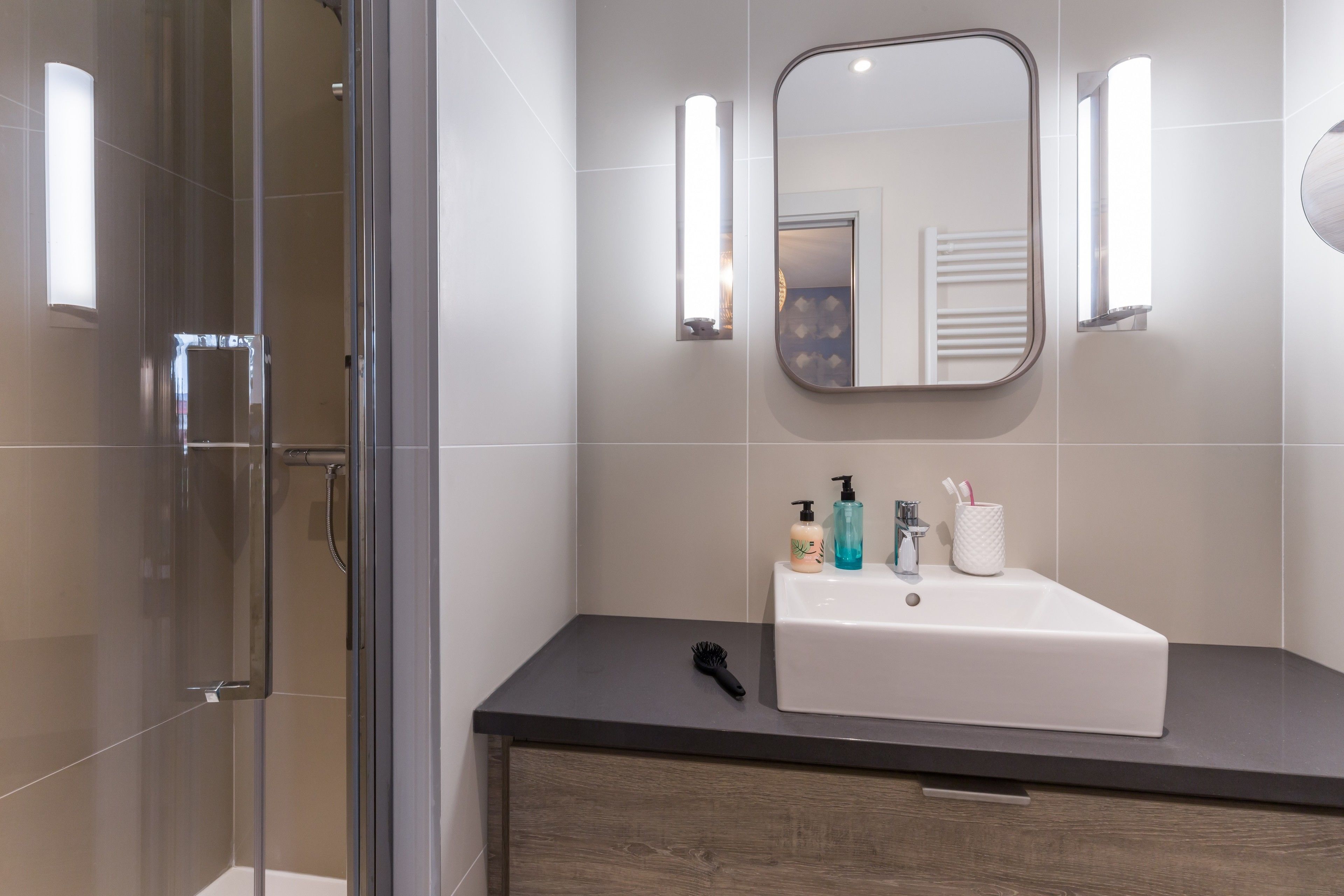 A modern bathroom with a glass shower enclosure, a white sink, and two wall-mounted lights.