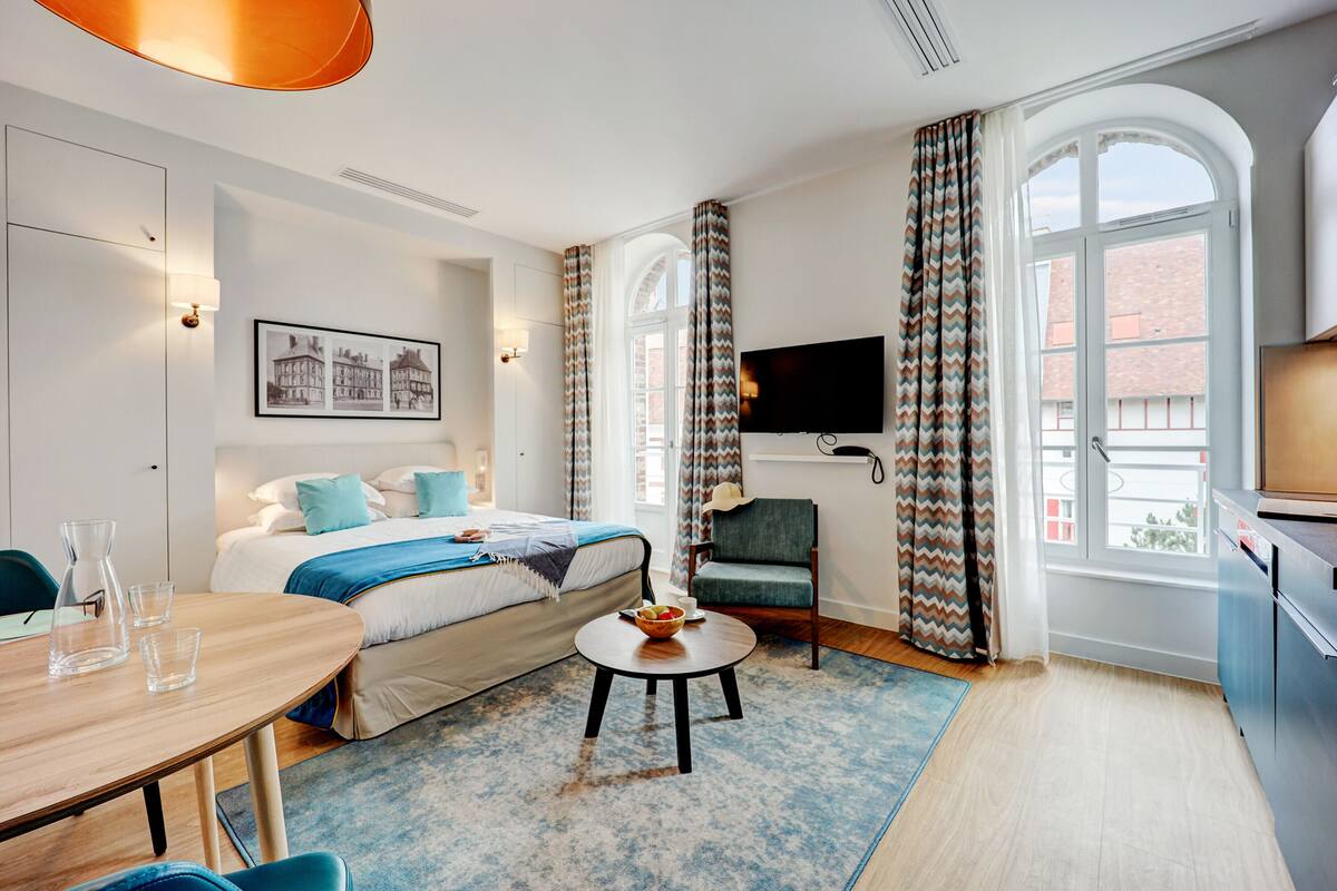 Quarto de hotel com cama, mesa de jantar, televisão e vista para a cidade.