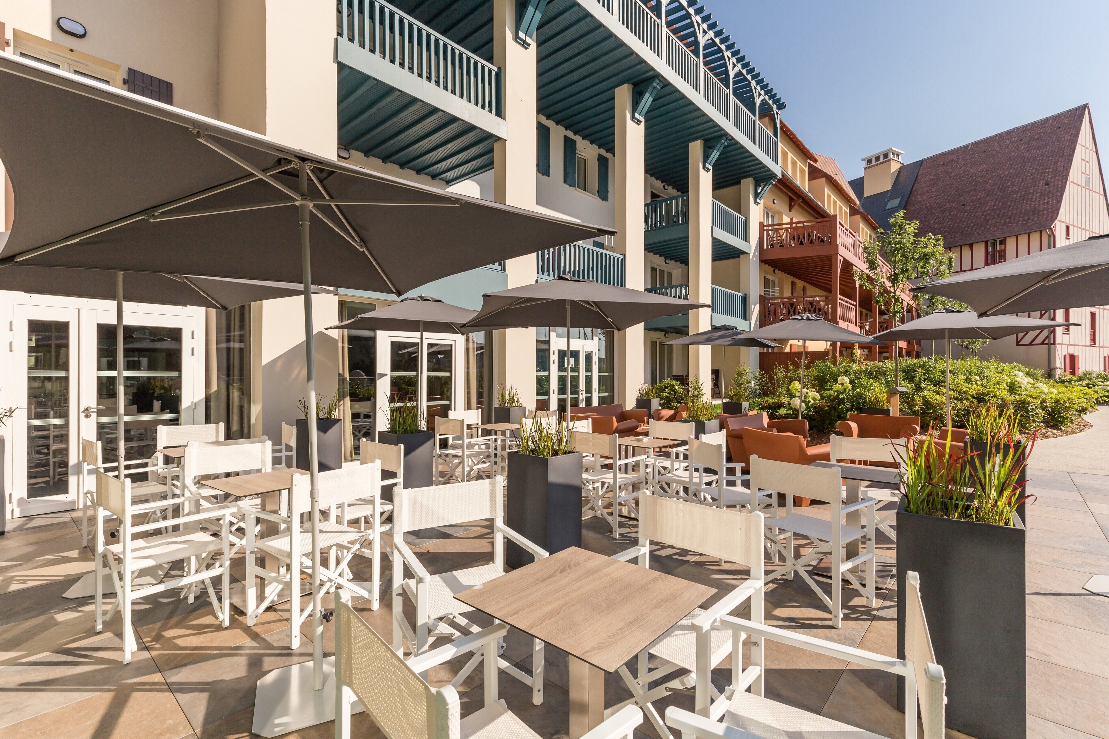 An outdoor patio with white tables and chairs, umbrellas, and potted plants.