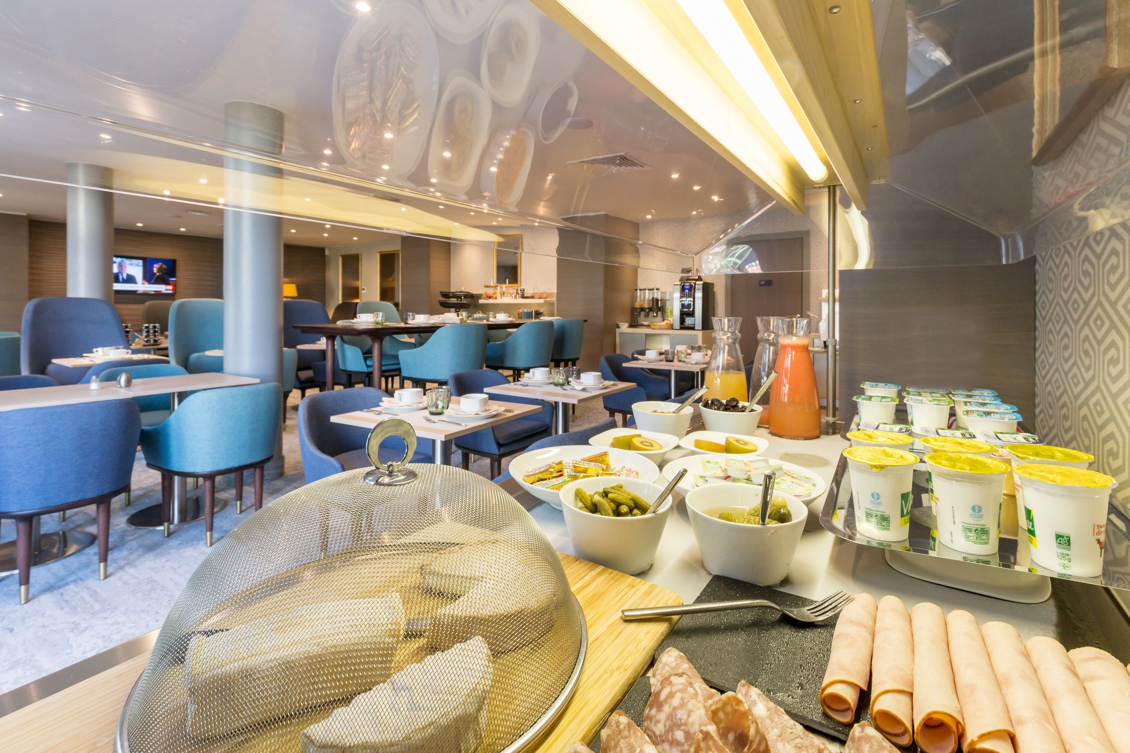 A hotel dining area with blue chairs, tables, and a buffet with various food items and drinks.