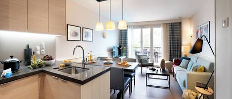 Cocina moderna con una isla central, comedor con sofá y sala de estar con televisor.