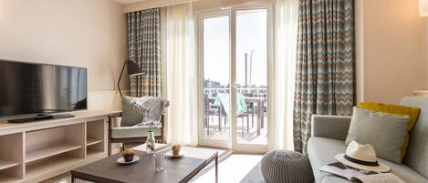 A modern living room with a flat-screen TV, a coffee table, a sofa, and a balcony with curtains.