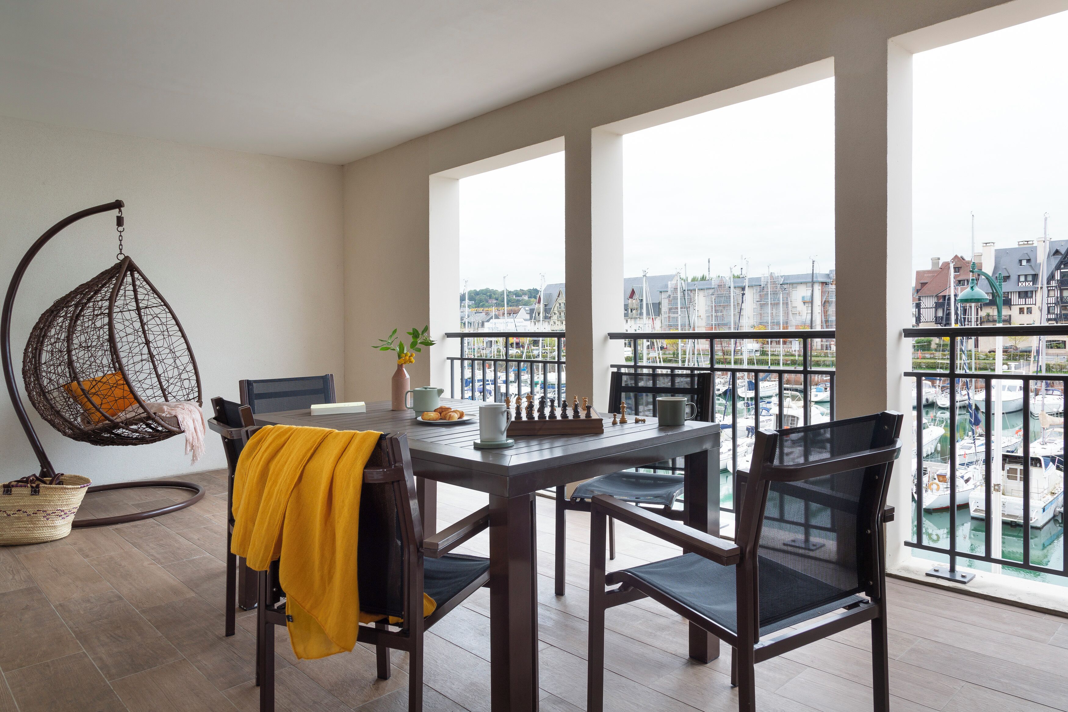 Un balcón con vista a un puerto deportivo, una silla colgante, una mesa de comedor con sillas y un tablero de ajedrez.