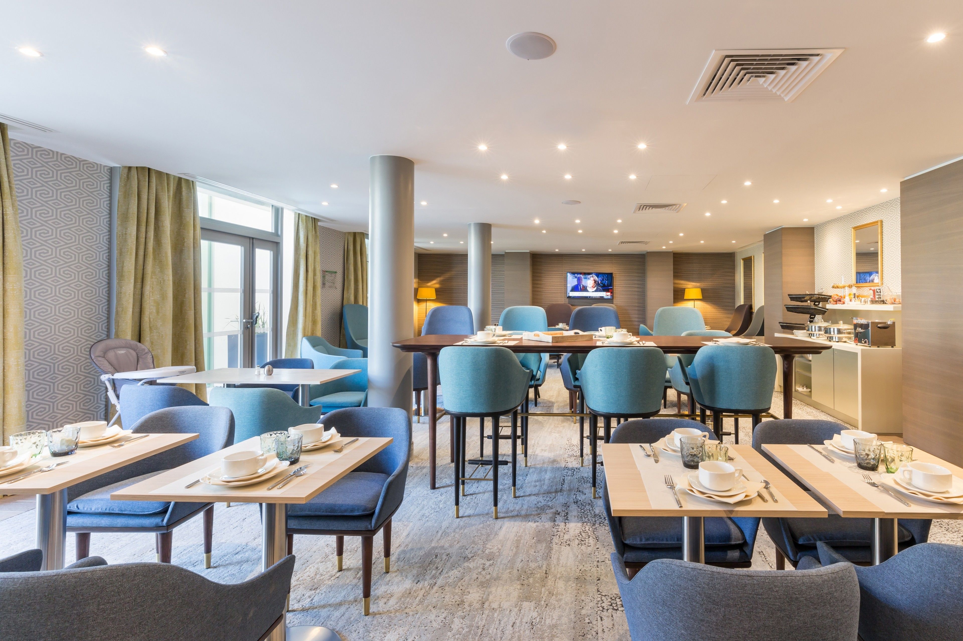 Un comedor moderno con mesas, sillas, televisor y zona de cocina.