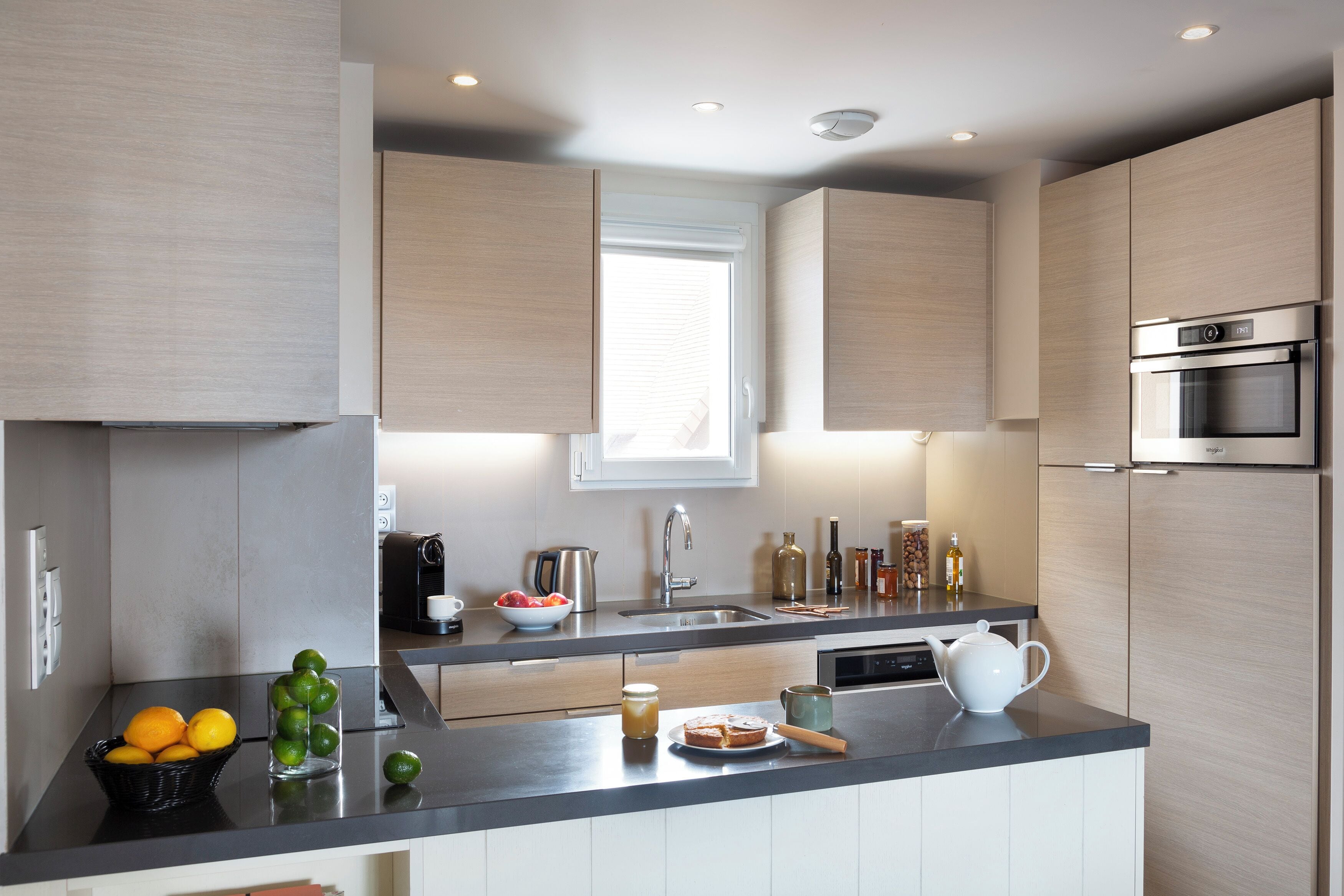 Una cocina moderna con un lavamanos de acero inoxidable, un horno empotrado y una ventana sobre el lavamanos.