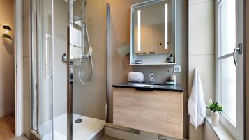 Een moderne badkamer met een douchecabine van glas, een houten wastafelmeubel, een grote spiegel en een raam voor natuurlijk licht.