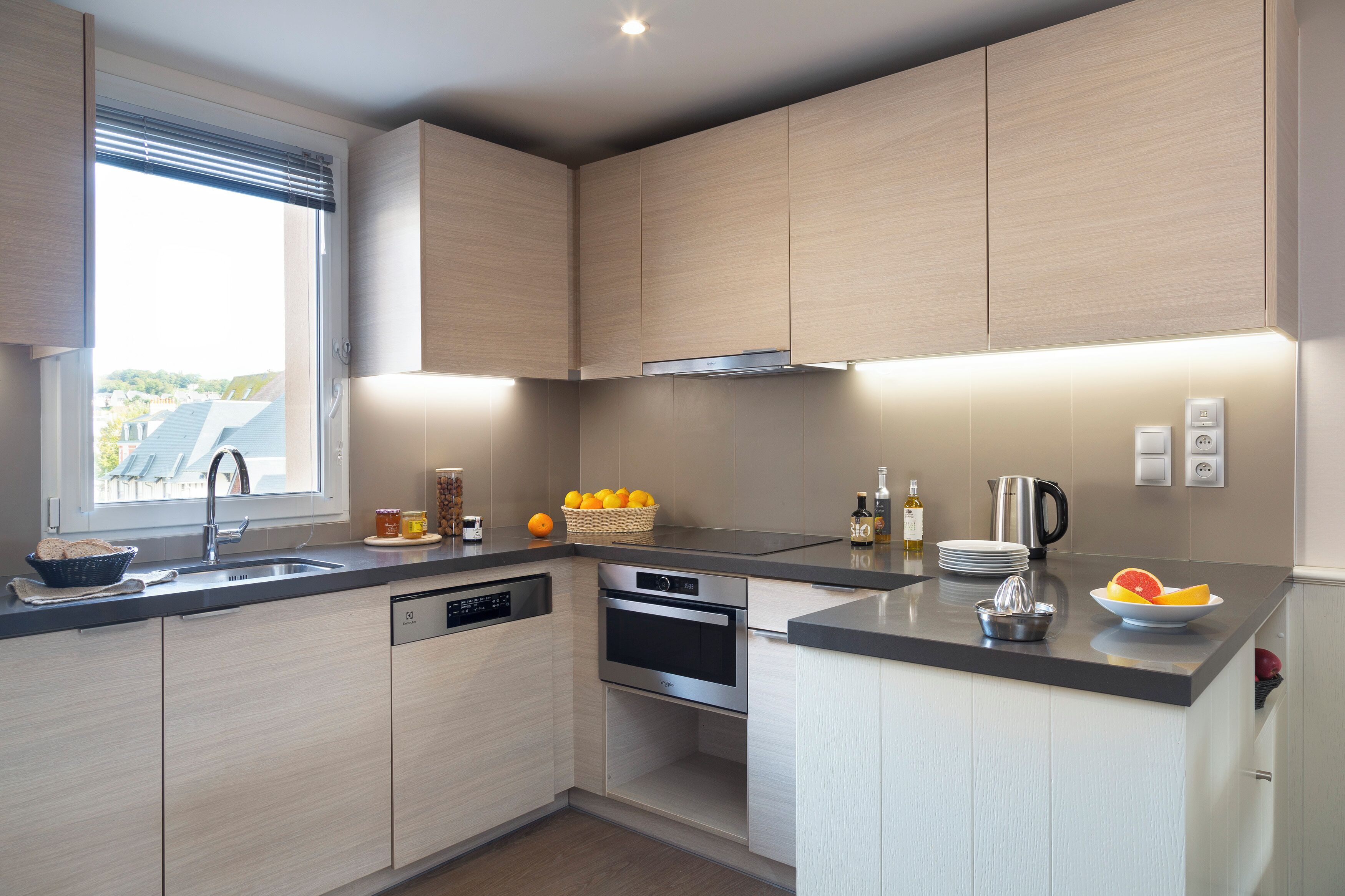 A modern kitchen with built-in appliances, a window with blinds, and a view of the outside.