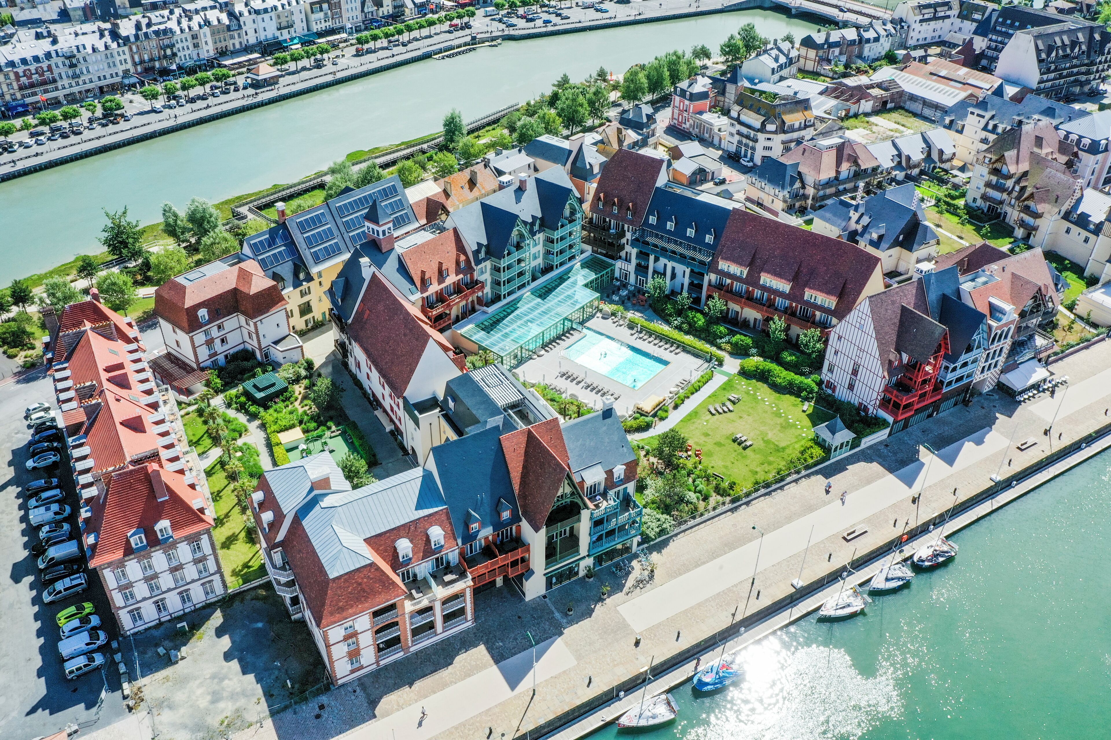 Vista aérea de un hotel a orillas del río, con varias edificaciones, una piscina y barcos amarrados.